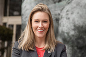 Danielle Blacklock is wearing a red shirt under a gray suit jacket.