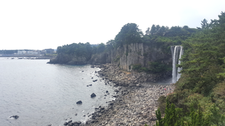 A rocky coastline with steep cliffs. A waterfall is seen spilling down from the cliffs to the rocky shore.