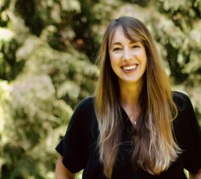 Olivia Zimmerman wears a black top and stands in front of green foliage.