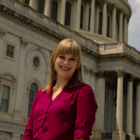 Megan McKeown, dressed in a fuschia button down shirt, is seen standing in front of the US House of Representatives.