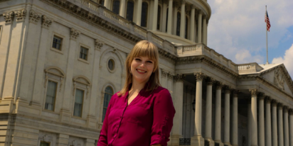 Megan McKeown, dressed in a fuschia button down shirt, is seen standing in front of the US House of Representatives.