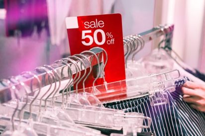 A rack of clothing hangs in a store with a large red tag that reading, "sale 50% off