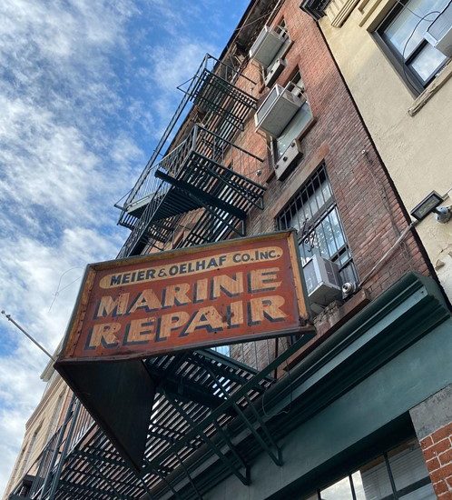Alt text: A rusted red sign on a brick building reads "Meier & Oelhaf Co. Inc., Marine Repair."
