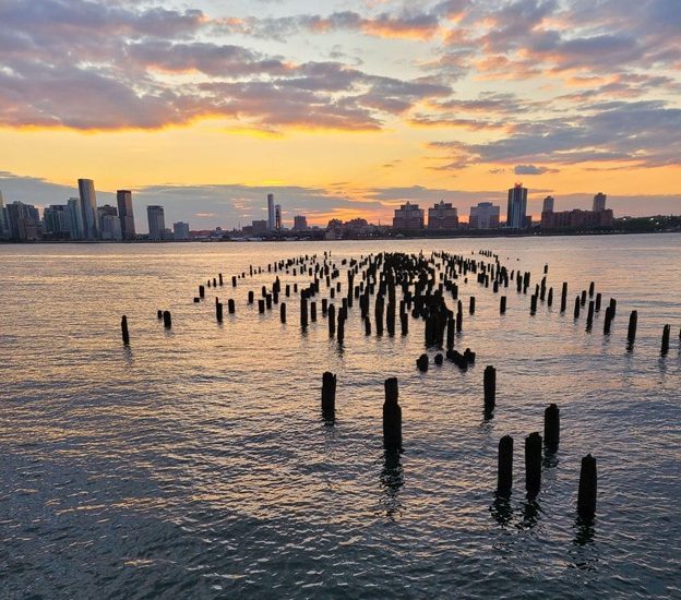 Pier pilings stick out of the river water at sunset, showing the area once covered by pier.