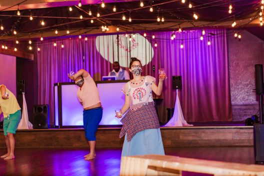 Leah Huff standing on a dance floor holding a glass of water in each hand.