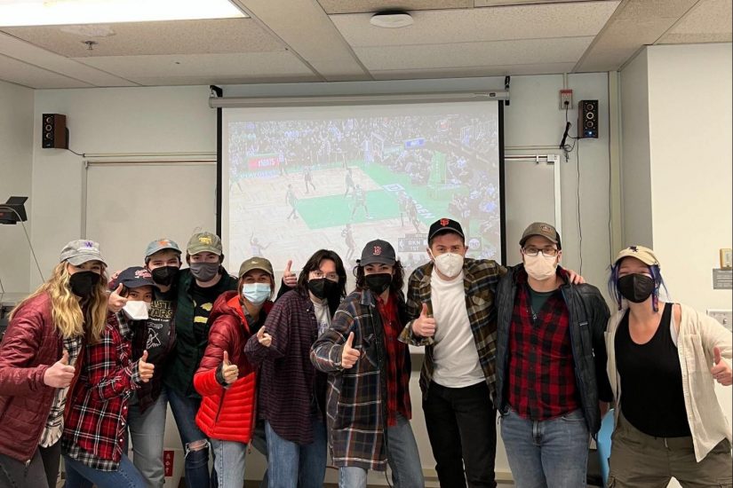 several members of EEL (Engaged Ethnography Lab) line up in front of a projector playing a basketball game; everyone is dressed similarly in flannels and hats to celebrate our advisor's birthday.