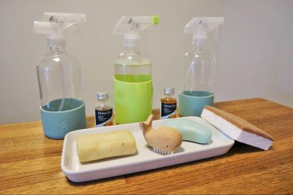 A lineup of 3 squirt bottles, and a tray of sustainable, "ecofriendly" cleaning products on a wooden table.