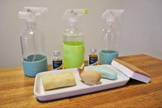 A lineup of 3 squirt bottles, and a tray of sustainable, "ecofriendly" cleaning products on a wooden table.