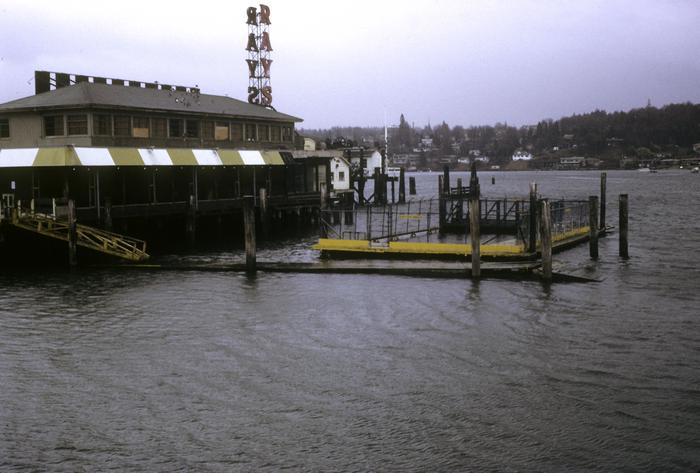 A one-story restaurant photographed from the water. The restaurant sits on a dock. A neon red "RAY'S" sign sticks up from one corner of the restaurant.
