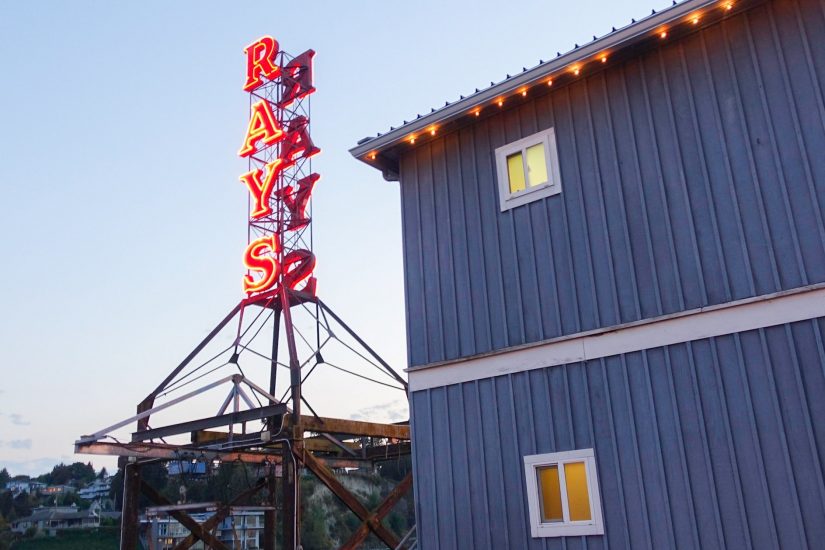 A neon red "RAY'S" sign sticks up next to a blue-grey building.