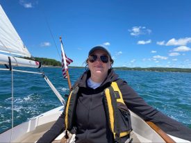 Amelia steers a sail boat on a body of water with islands in the background