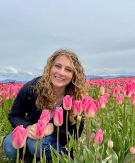 Maddie kneels in a field of pink tulips