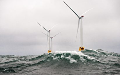 Waves crest in front of 3 Halide 6 MW wind turbines under cloudy skies. The mono-pile windmills are a part of the Block Island Wind Farm off the shores of Rhode Island.