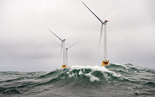Waves crest in front of 3 Halide 6 MW wind turbines under cloudy skies. The mono-pile windmills are a part of the Block Island Wind Farm off the shores of Rhode Island.