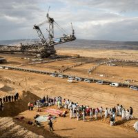 In Germany, lines of people stand at a coal mine and block a large piece of heavy mining machinery.