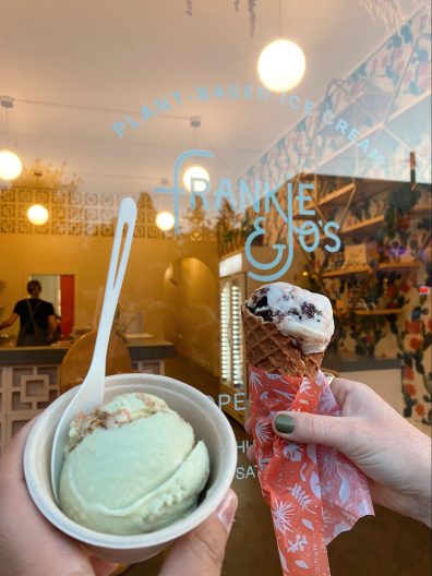 Hand holding Siete’s carlota de limón in a cup on the left and hand holding mint brownie in a waffle cone on the right in front of the Frankie & Jo's clear glass door.