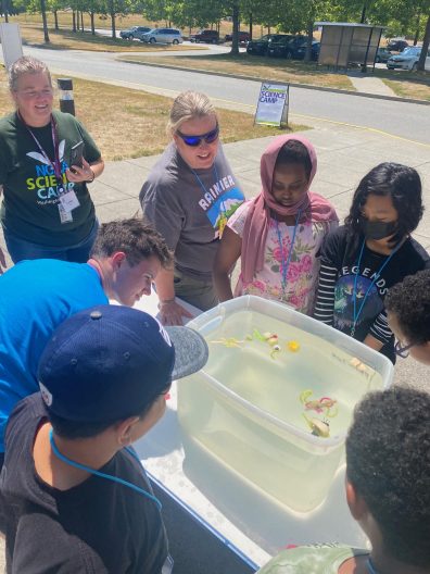 Camp staff, teacher chaperones, and camper submerge their "plankton" in a bucket of water during the "The Great Plankton Race."