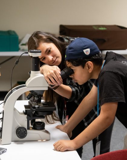 Accompanied by a scientist, a middle school camper looks through a microscope at phytoplankton.