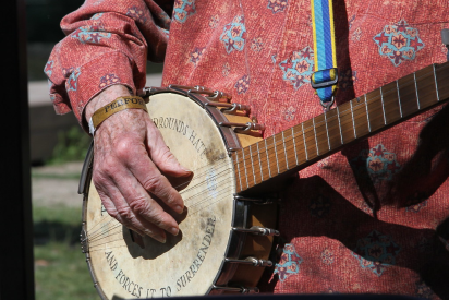 A close up photo of Pete Seeger’s hand on a banjo with the words “This machine surrounds hate and forces it to surrender'' printed on the head of the banjo.