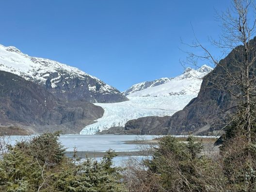The once mighty Mendenhall glacier emptys into a frozen lake and sits at the base of a large grey mountain.