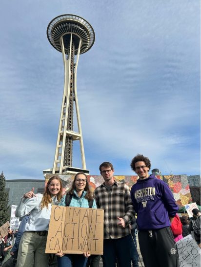 Four graduate students standing in front of the Space Needle holding a sign that says "Climate Action Can't Wait".