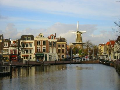 a photo of a town in the Netherlands with a river flowing through and a windmill in the for ground