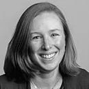 Smiling woman with shoulder-length hair in black and white photo. She wears a blazer and exudes a friendly, approachable demeanor against a plain background.