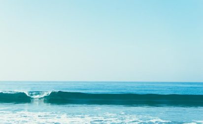 Calm ocean waves under a clear blue sky, conveying tranquility and serenity. The horizon separates the vibrant blue sea from the pale sky above.